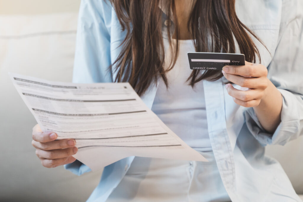 Woman holding a credit card in one hand and a bill in the other while reviewing finances.