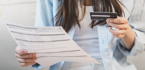 Woman holding a credit card in one hand and a bill in the other while reviewing finances.