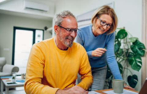 Senior middle aged happy couple using laptop together at home.