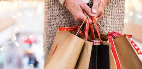 Older adult holding several holiday shopping bags in a mall.