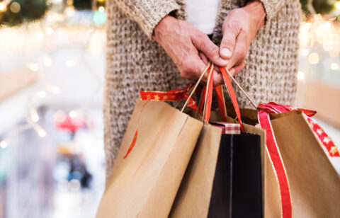 Older adult holding several holiday shopping bags in a mall.