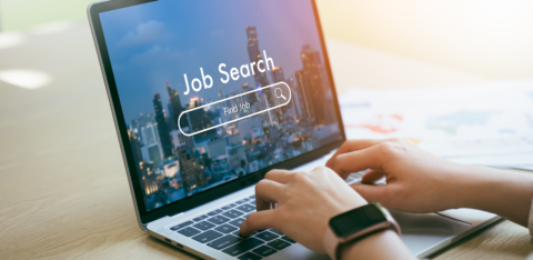Person typing on a laptop with a “Job Search” screen displayed, showing a cityscape background.