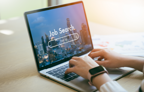 Person typing on a laptop with a “Job Search” screen displayed, showing a cityscape background.