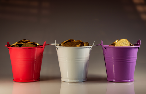 Metal buckets in red, white, and purple, each overflowing with gold coins against a neutral background.