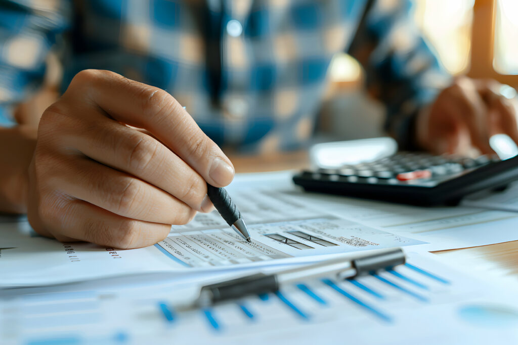 Close-up of a person analyzing financial documents with a pen in hand and a calculator nearby on a desk.
