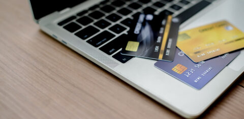 Several credit cards spread across a laptop keyboard on a wooden desk