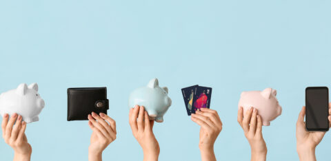 Multiple hands holding piggy banks, a wallet, credit cards, and a smartphone against a pastel blue background