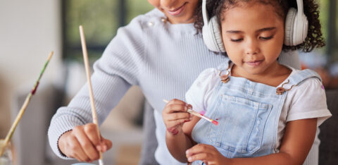 Mother and daughter painting together at home, with the child wearing headphones while creating artwork.