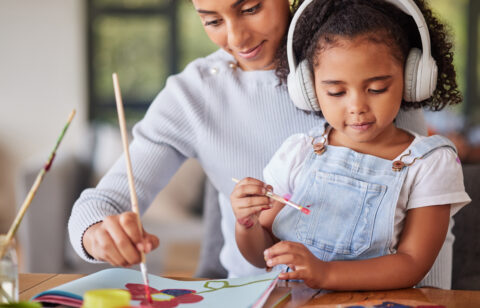 Mother and daughter painting together at home, with the child wearing headphones while creating artwork.