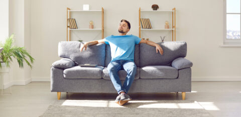 Relaxed young man is enjoying free time and sitting on comfortable couch at home