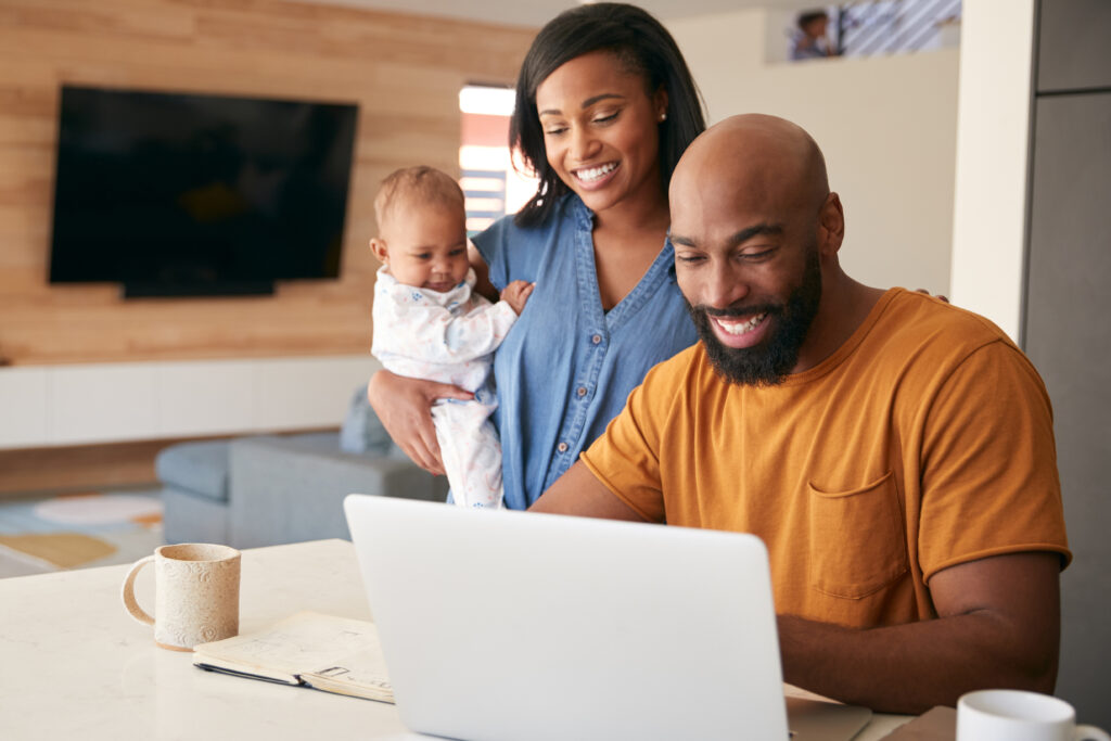 A smiling couple with their baby looking at a laptop together in a modern living room.