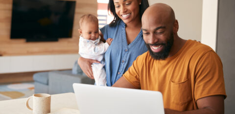 A smiling couple with their baby looking at a laptop together in a modern living room.