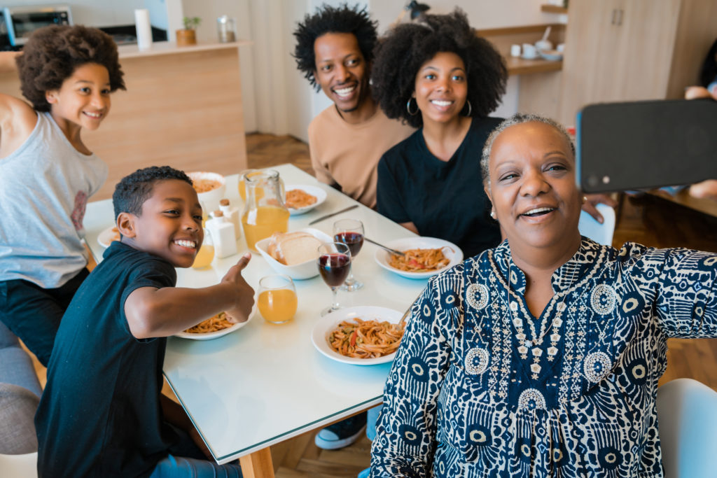 Five members of a multigenerational household pose at the dinner table to take a picture.