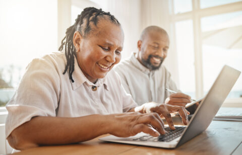 Senior couple looking at computer and filling out notepad