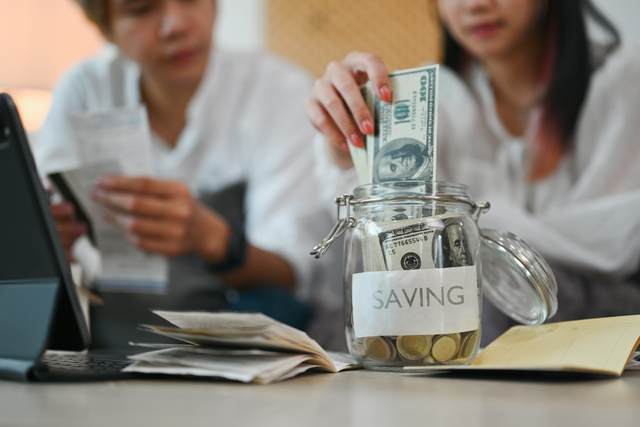 young couple putting money into a savings jar.