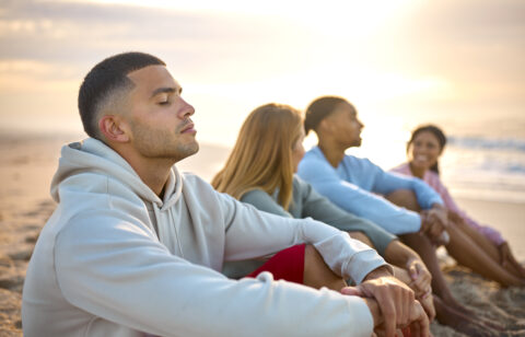 Man With Closed Eyes Relaxing With Friends On Vacation Sitting on beach thinking bout financial independence