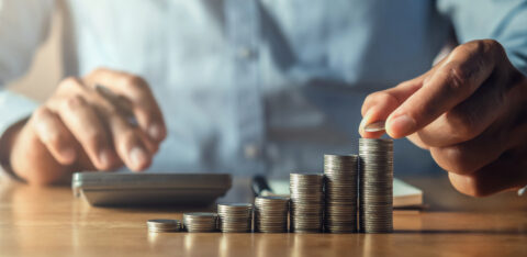 Close-up of a person stacking coins in ascending order while using a calculator, symbolizing financial growth and savings.