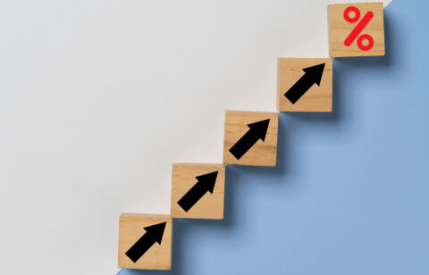 Wooden blocks arranged in a staircase pattern with black upward arrows, leading to a final block with a red percentage symbol, symbolizing financial growth.