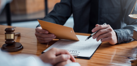 Lawyer reviewing a legal document with a client, holding an envelope and a pen at a wooden desk.