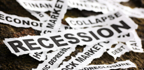 Torn newspaper clippings with economic crisis-related words such as "Recession," "Stock Market," "Collapse," and "Debt" scattered on a rough surface.