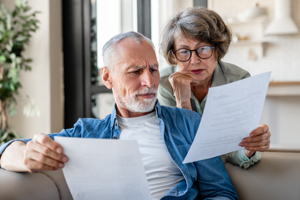 Concerned senior couple sitting on a couch reviewing financial documents together.