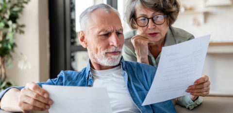 Concerned senior couple sitting on a couch reviewing financial documents together.