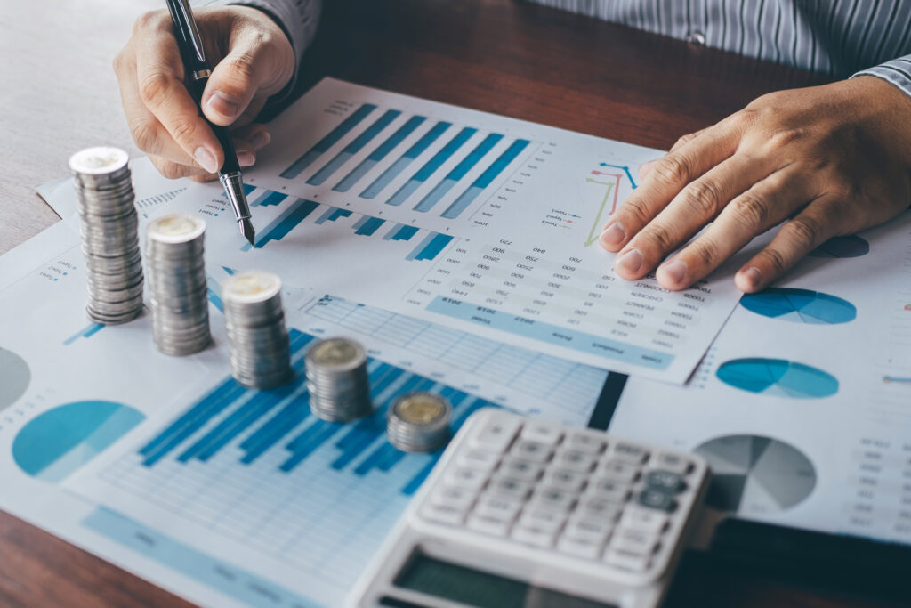 Close-up of a person analyzing financial charts with stacked coins and a calculator on the desk.