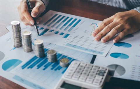 Close-up of a person analyzing financial charts with stacked coins and a calculator on the desk.