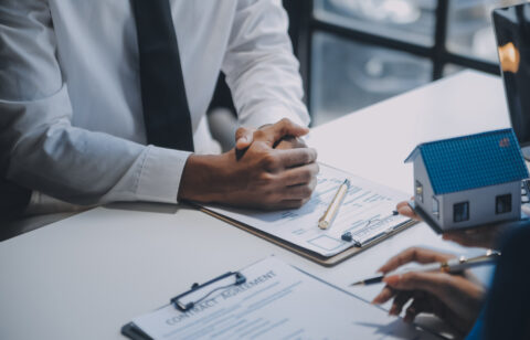 Agent and client discussing a contract with a miniature house model on the table.