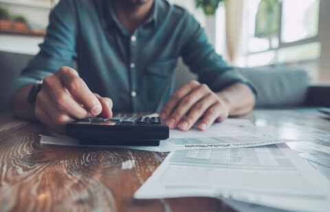 Close-up of a person using a calculator while reviewing financial documents on a wooden table.