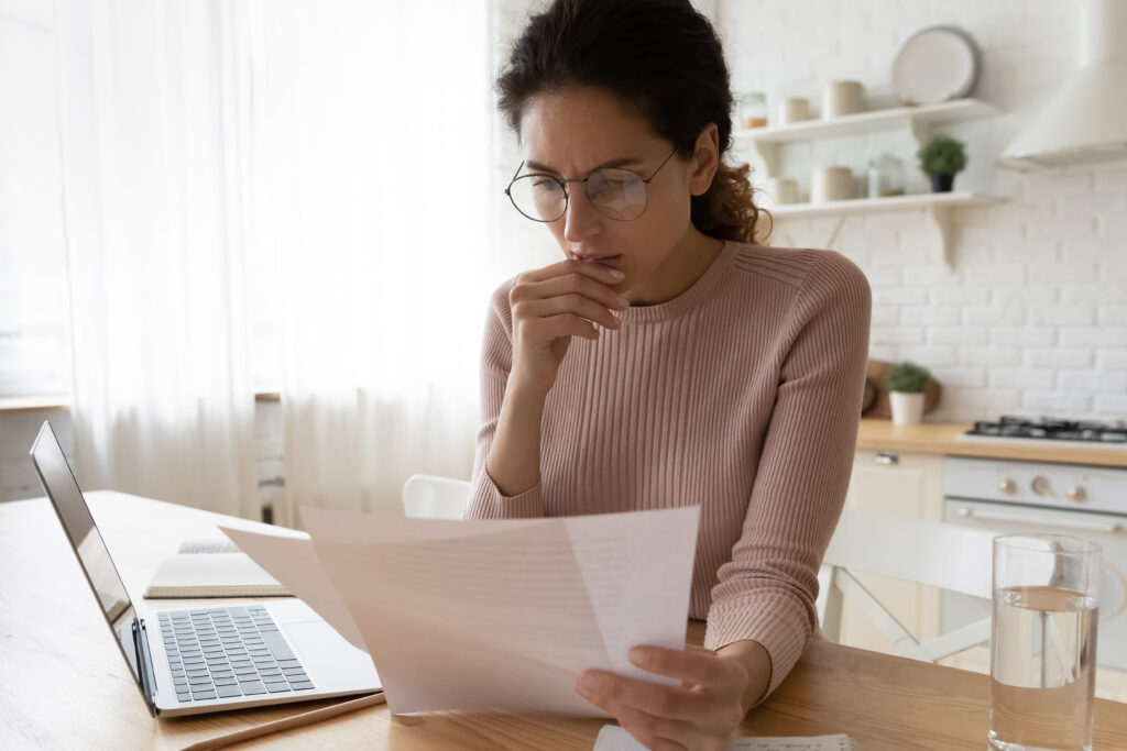 woman looking at computer and paper bills