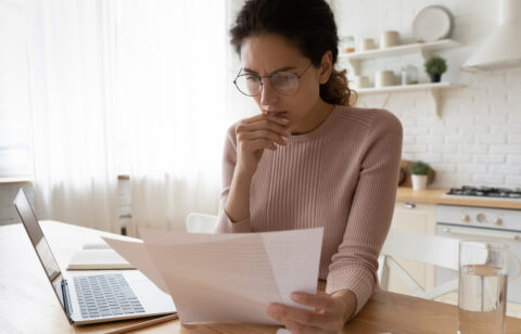 woman looking at computer and paper bills