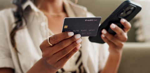 Woman holding a credit card in one hand and a smartphone in the other, possibly making an online purchase.