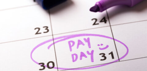 Close-up of a calendar with "PAY DAY" written in purple marker on the 31st, circled with a smiley face, alongside an open marker.