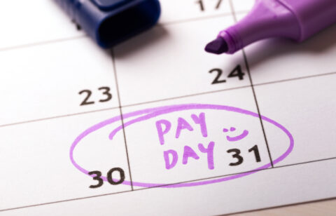 Close-up of a calendar with "PAY DAY" written in purple marker on the 31st, circled with a smiley face, alongside an open marker.