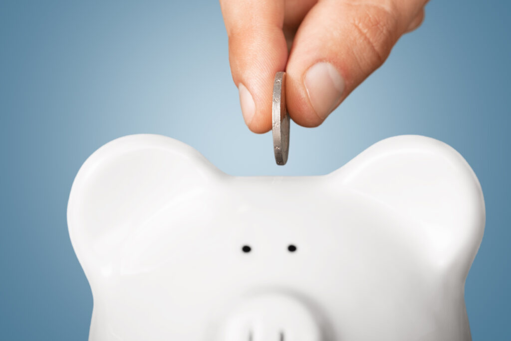 Close-up of a hand inserting a coin into a white piggy bank