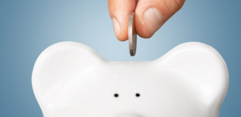 Close-up of a hand inserting a coin into a white piggy bank