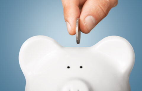 Close-up of a hand inserting a coin into a white piggy bank
