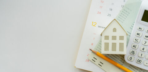 A calendar, miniature house model, calculator, and financial documents arranged on a desk, symbolizing mortgage planning and homeownership.
