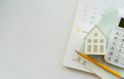A calendar, miniature house model, calculator, and financial documents arranged on a desk, symbolizing mortgage planning and homeownership.