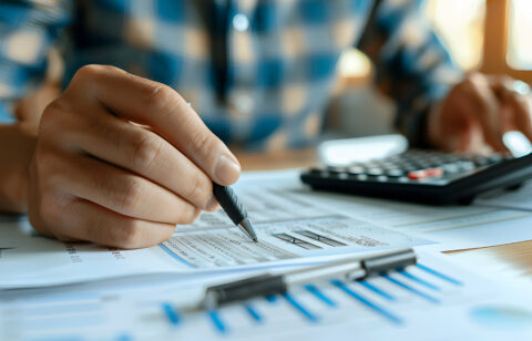 Close-up of a person analyzing financial documents with a pen and calculator.