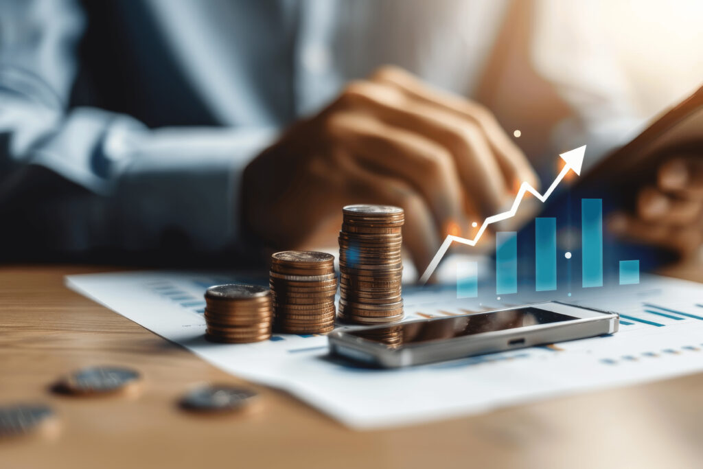 Stacks of coins on financial documents with a smartphone and a digital growth chart overlay