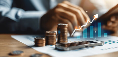 Stacks of coins on financial documents with a smartphone and a digital growth chart overlay