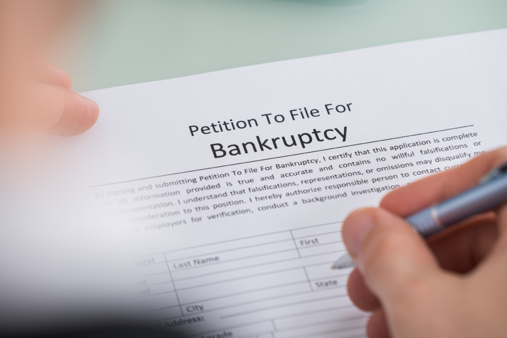 Close-up of a person filling out a petition to file for bankruptcy form with a pen.