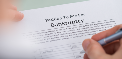 Close-up of a person filling out a petition to file for bankruptcy form with a pen.