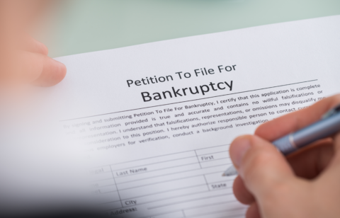 Close-up of a person filling out a petition to file for bankruptcy form with a pen.