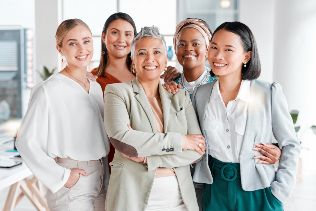 A diverse group of confident professional women smiling together in a modern office setting.