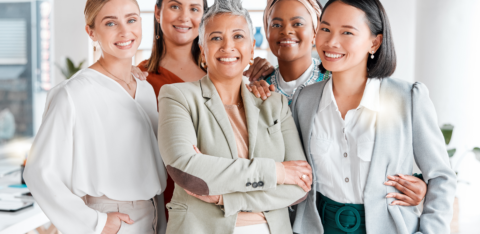 A diverse group of confident professional women smiling together in a modern office setting.