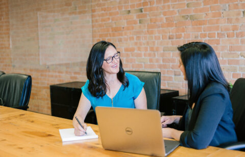 Two professional women having a friendly conversation during a meeting in a modern office.