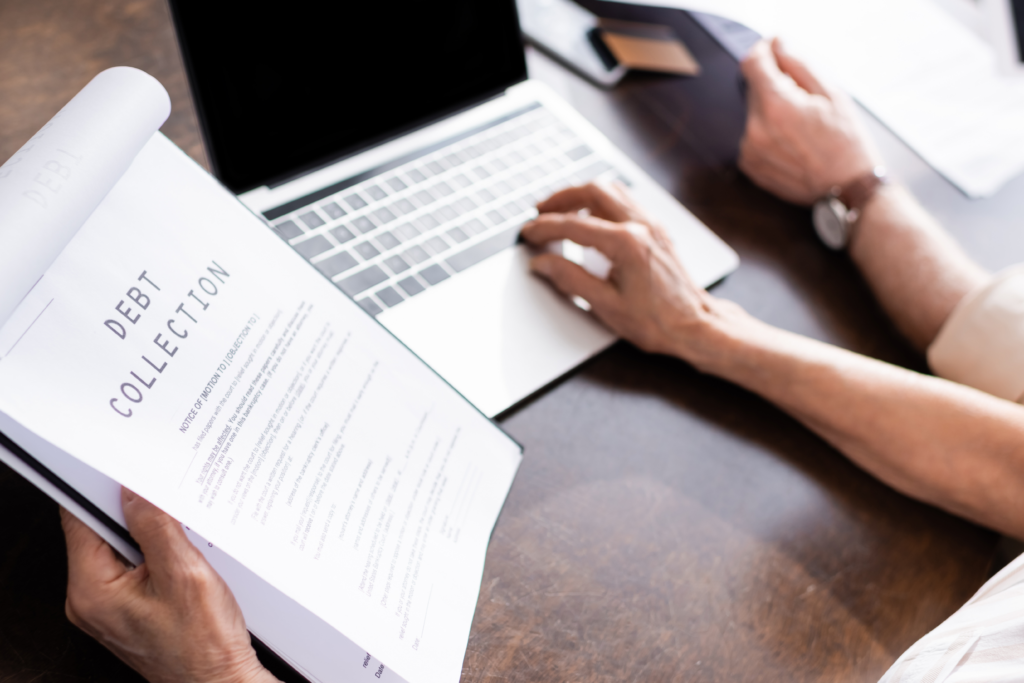 Person reviewing a debt collection notice while using a laptop at a desk